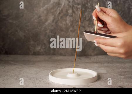 Bâton d'Encens dans un support en céramique d'artisanat en porcelaine sur une table en marbre. Méditation et concept de yoga. Main de womans avec de longs allumettes pour brûler l'encens Banque D'Images