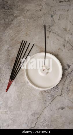 Bâton d'Encens dans un support en céramique d'artisanat en porcelaine sur une table en marbre. Bâtonnets d'arôme. Méditation et concept de yoga. Photo verticale sur fond de marbre Banque D'Images