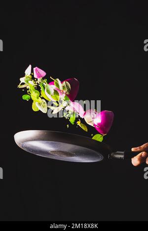 Fabrication de ceviche de style brésilien sur fond noir. Poêle à frire jeter des ingrédients comme l'oignon rouge, le fromage, le basilic et les assaisonnements dans l'air. Banque D'Images