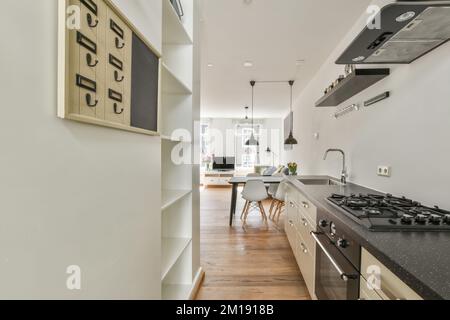 une longue cuisine étroite avec des murs blancs et du parquet, ainsi que des comptoirs en granit noir de chaque côté Banque D'Images