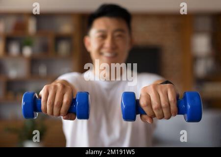 Sportif coréen mature homme dans sportswear s'exerçant seul à la maison, en utilisant des cloches bleues, travaillant sur la force des bras Banque D'Images