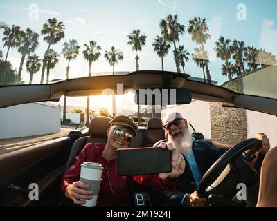 Couple senior s'amuser à faire du selfie à l'intérieur d'une voiture convertible pendant les vacances - concept de voyage pour les personnes âgées Banque D'Images