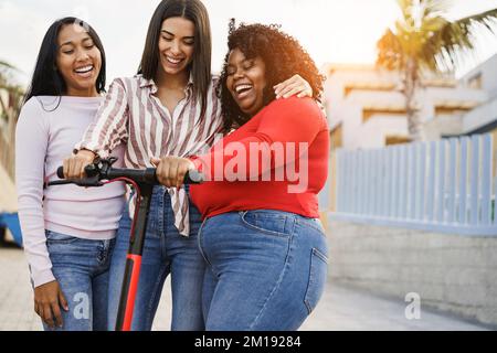 Joyeux multiethnique filles ayant l'amusement avec le scooter électrique en plein air - Focus sur le visage de fille africaine Banque D'Images