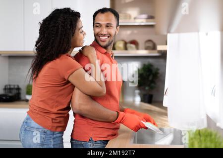 Nettoyage à temps libre à la maison. Bonne jolie jeune femme noire qui embrasse l'homme dans des gants en caoutchouc Banque D'Images