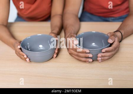 Crise mondiale et famine. Les mains de l'épouse noire millénaire et de son mari en t-shirts tiennent des assiettes vides sur la table Banque D'Images