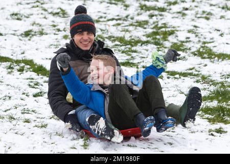 Chippenham, Wiltshire, Royaume-Uni, 11th décembre 2022. Alors que les habitants de Chippenham se réveillent devant leur première neige de l'année, un homme et un enfant sont photographiés dans un parc local de Chippenham lorsqu'ils glissent sur une colline sur un traîneau. Credit: Lynchpics/Alamy Live News Banque D'Images