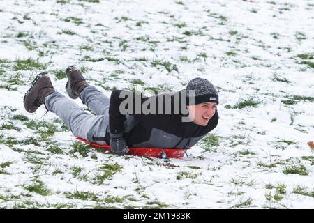 Chippenham, Wiltshire, Royaume-Uni, 11th décembre 2022. Alors que les habitants de Chippenham se réveillent devant leur première neige de l'année, un homme est photographié dans un parc local de Chippenham alors qu'il descend une colline sur un traîneau. Credit: Lynchpics/Alamy Live News. Banque D'Images