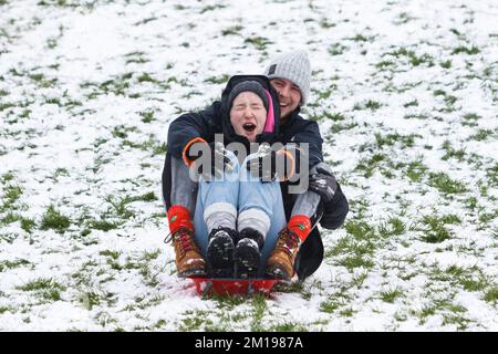 Chippenham, Wiltshire, Royaume-Uni, 11th décembre 2022. Alors que les habitants de Chippenham se réveillent devant leur première neige de l'année, deux personnes sont photographiées dans un parc local de Chippenham alors qu'ils descendent une colline sur un traîneau. Credit: Lynchpics/Alamy Live News. Banque D'Images
