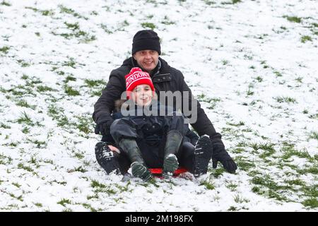 Chippenham, Wiltshire, Royaume-Uni, 11th décembre 2022. Alors que les habitants de Chippenham se réveillent devant leur première neige de l'année, un homme et un enfant sont photographiés dans un parc local de Chippenham lorsqu'ils glissent sur une colline sur un traîneau. Credit: Lynchpics/Alamy Live News Banque D'Images
