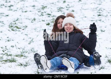 Chippenham, Wiltshire, Royaume-Uni, 11th décembre 2022. Alors que les habitants de Chippenham se réveillent devant leur première neige de l'année, deux enfants sont photographiés dans un parc local de Chippenham alors qu'ils descendent une colline sur un traîneau. Credit: Lynchpics/Alamy Live News. Banque D'Images