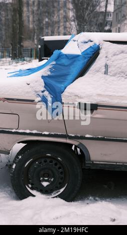 pare-brise arrière cassé d'une voiture après un accident en hiver. un trou dans le pare-brise arrière d'une voiture et recouvert d'une bâche bleue. la glace de la voiture est cassée Banque D'Images