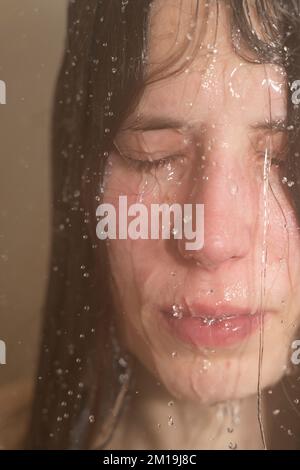 Jeune femme sous la douche avec de l'eau qui coule le long de son visage. Concept : santé mentale, détresse, sentiment cassé, trouble dysmorphique du corps Banque D'Images