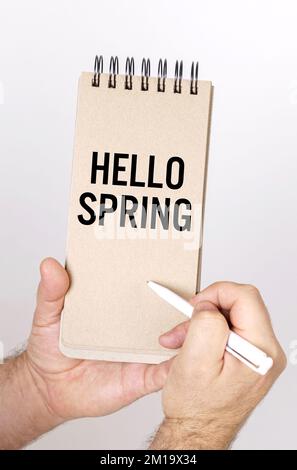 Concept de personnes et de vacances. Un homme tient dans ses mains un stylo et une chatter avec l'inscription - Hello Spring Banque D'Images