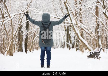 Femme portant une veste en duvet debout avec ses mains levées et profitant du temps enneigé. Loisirs dans le parc d'hiver, saison froide Banque D'Images