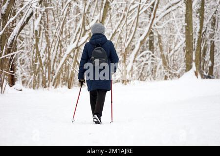 Marche nordique par temps froid, mode de vie sain. Femme avec des bâtons marche dans le parc d'hiver sur fond d'arbres couverts de neige Banque D'Images