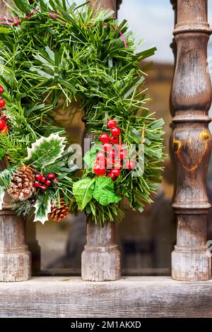 Couronne décorative de Noël avec branches de sapin et cônes de pin et baies de houx rouges sur une porte ornementale en bois Banque D'Images