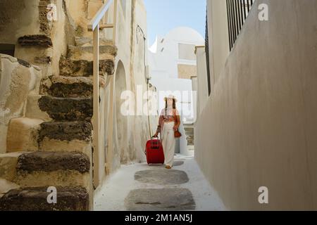 Une jeune femme avec une valise rouge traverse les vieilles rues de Grèce Banque D'Images