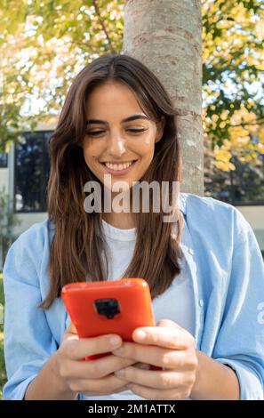 Jeune femme souriante discutant avec un smartphone dans un parc Banque D'Images