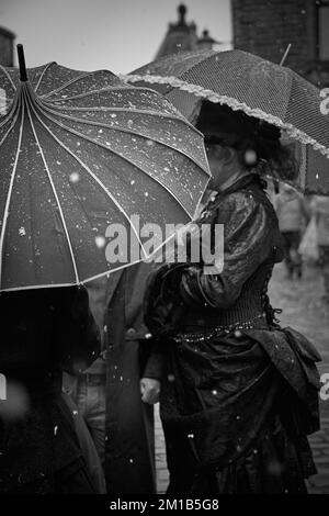 Un groupe de femmes vêtues de vêtements victoriens pour un événement Steampunk à Haworth, dans le West Yorkshire, se protège de la neige sous des parasols décoratifs Banque D'Images