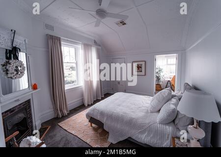 Un grand angle de la chambre lumineuse avec un lit blanc, une cheminée sous le miroir avec une couronne, et une image murale au milieu des portes Banque D'Images