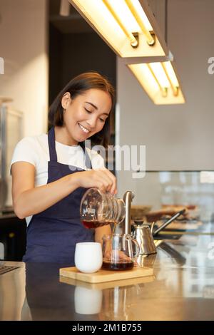 Jolie femme de barista coréenne, en versant du café, en préparant du filtre en lot, en le distribuant, en travaillant dans un café Banque D'Images