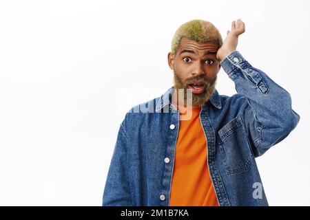 Portrait de l'homme de style afro-américain, semble choqué, touche sa tête et fixe en incrédulité à l'appareil photo, se tient sur fond blanc Banque D'Images