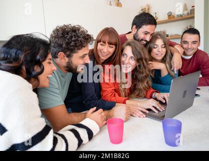 Un grand groupe d'amis caucasiens ayant la conversation autour d'un ordinateur portable dans un salon de l'auberge moderne Banque D'Images