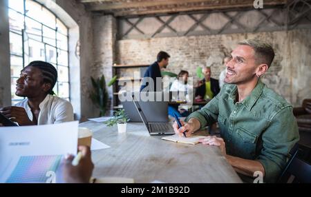 Homme créatif enthousiaste prenant des notes au sujet d'une nouvelle campagne de marketing - Portrait de bonheur homme sourire tout en écoutant une réunion sur le bureau - Cowork Banque D'Images