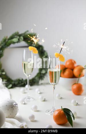 Quelques minutes avant une nouvelle année. Deux verres de champagne et de mandarines sur une table décorée de boules de noël et de couronne. Banque D'Images