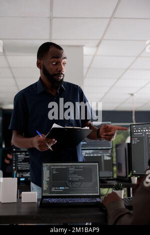 Développeur web afro-américain analysant le script html sur la fenêtre du terminal, en utilisant la base de données du serveur sur l'ordinateur. Les codeurs discutent du langage de programmation et de l'interface utilisateur du cloud computing. Banque D'Images