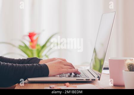 Gros plan des mains d'une femme touchant le clavier de son ordinateur portable sur son bureau à la maison. Banque D'Images