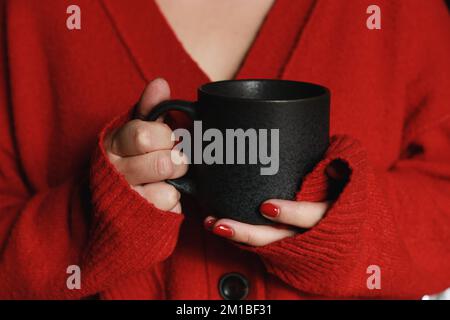 gros plan des mains des femmes tenant une tasse de café grise, portant un pull doux et chaud rouge Banque D'Images