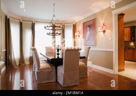 Table en bois avec chaises rembourrées à haut dossier dans la salle à manger avec lustre de style médiéval et plancher de bois franc verni à l'intérieur de la maison luxueuse. Banque D'Images