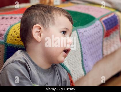 Jeune garçon expressif regardant des dessins animés dans la salle de séjour Banque D'Images