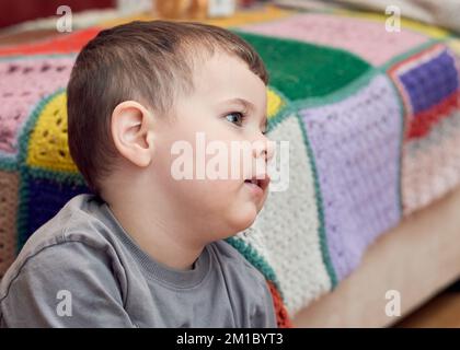 Jeune garçon expressif regardant des dessins animés dans la salle de séjour Banque D'Images