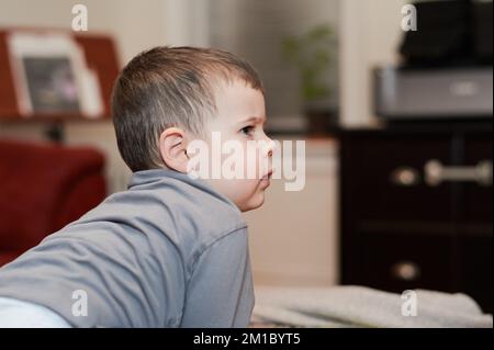 Jeune garçon expressif regardant des dessins animés dans la salle de séjour Banque D'Images