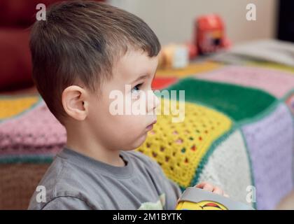 Jeune garçon expressif regardant des dessins animés dans la salle de séjour Banque D'Images