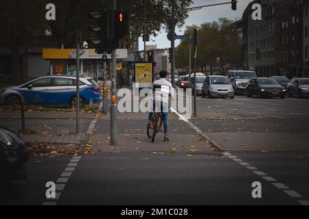 Photo d'un jeune homme à vélo, qui attend de traverser une rue où les voitures circulent à Aix-la-Chapelle, en Allemagne. Banque D'Images
