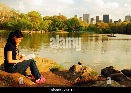 Une jeune femme aime lire un livre dans le Central Park de New York, avec l'horizon animé de la ville en arrière-plan Banque D'Images