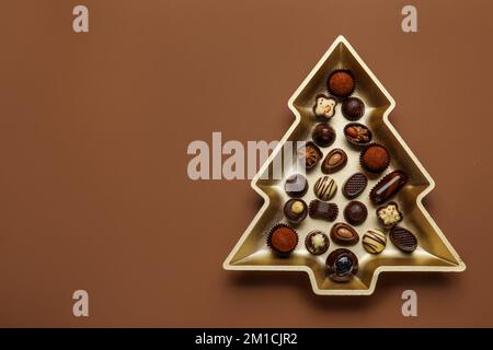 Assiette en forme d'arbre de Noël avec bonbons au chocolat sur fond marron Banque D'Images