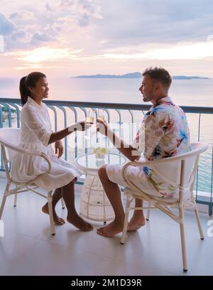 Quelques hommes blancs et femmes thaïlandaises boivent des cocktails sur le balcon d'un hôtel à Pattaya en Thaïlande au coucher du soleil. Banque D'Images