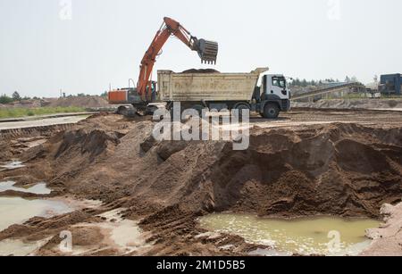 Sur le chantier, de grandes machines de travail - une pelle à chenilles orange et un camion à benne basculante gris en cours de travail - chargent le sol depuis la fosse Banque D'Images