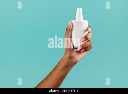 Crop anonyme afro-américaine femme démontrant plastique blanc produit cosmétique contre fond turquoise Banque D'Images