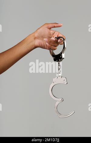 Crop anonyme afro-américaine de démonstration de menottes de police en métal ouvert sur fond gris Banque D'Images