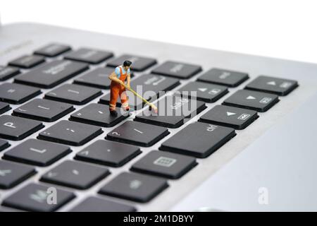 Photographie miniature de personnage de jouet de personnes. Les travailleurs balayeurs nettoient le clavier de l'ordinateur portable à l'aide d'un balai, d'une brosse. Isolé sur fond blanc. Image pho Banque D'Images