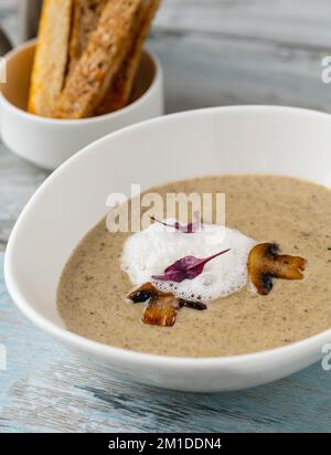 Crème de champignons dans un bol en porcelaine blanche sur une table en bois Banque D'Images