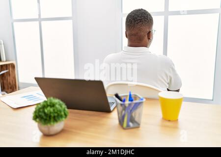 Jeune africain travaillant au bureau à l'aide d'un ordinateur portable debout en arrière regardant loin avec des bras croisés Banque D'Images
