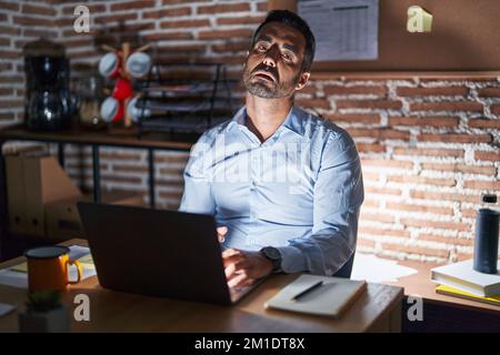 Homme hispanique avec la barbe travaillant au bureau la nuit regardant endormi et fatigué, épuisé pour la fatigue et la gueule de bois, les yeux paresseux le matin. Banque D'Images