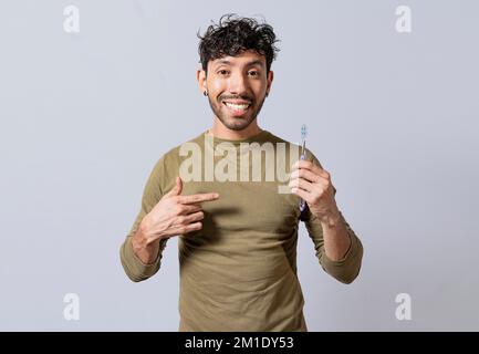 Homme souriant tenant et pointant vers la brosse à dents. Un homme charmant tenant et pointant vers la brosse à dents isolé. Personne tenant et pointant une brosse à dents Banque D'Images