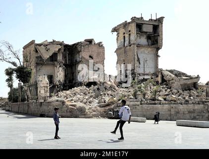 Deux garçons jouant avec une balle sur la place en face de la citadelle, à côté d'un bâtiment détruit du gouvernement du Grand Serail, Alep, en Syrie Banque D'Images